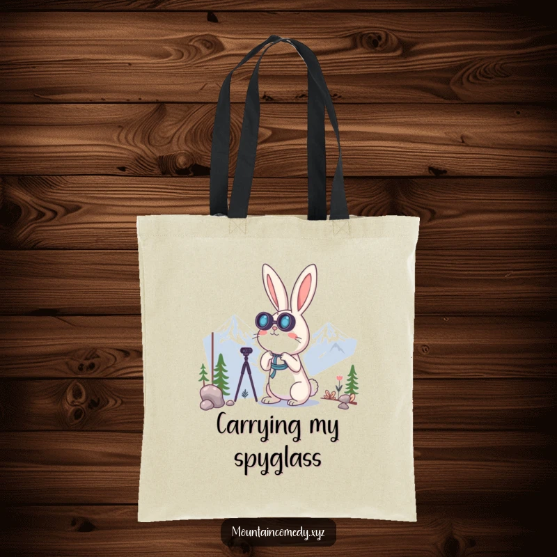 Funny rabbit character using binoculars to look at distant mountains, featured on a practical and humorous tote bag for explorers.